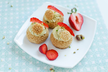 French traditional Choux pastry balls with pistachio cream and fresh strawberries on white plate on green background