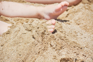 Stuck baby feet in sand on sea beach on sunny day.