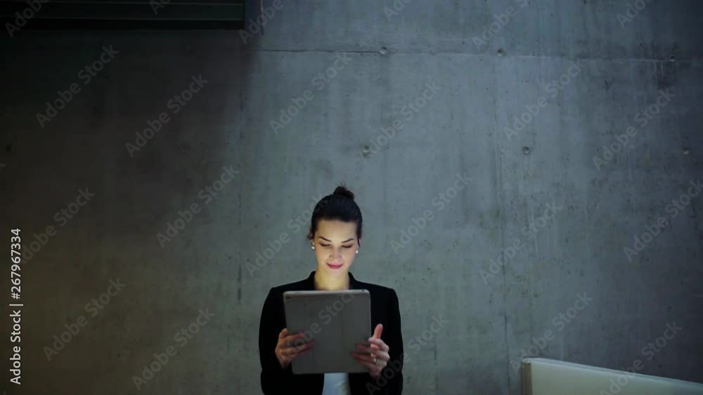 Wall mural Young business woman with tablet walking in office, concrete wall in background.