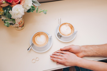 male hands are holding female hands. female hand with a wedding ring. reliable male hands. strong male hands. two cups of cappuccino. morning cappuccino. perfect morning