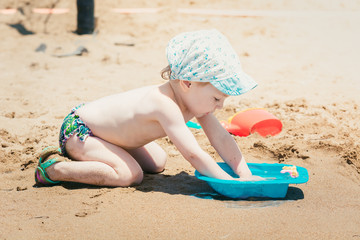 Nice baby in summer cap plays with toys on sandy beach.