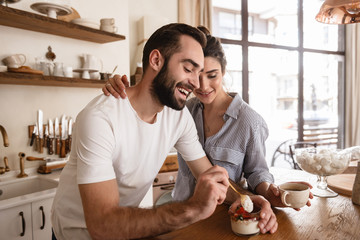 Photo of lovely brunette couple drinking coffee and eating desserts during breakfast in kitchen at...