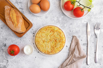 .Tortilla, Spanish omelette made with eggs and potatoes. Traditional Spanish tapas or snack served in white plate with cutlery and napkin. on cement table.