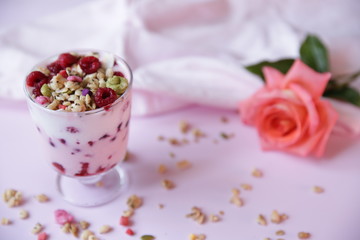 Granola yogurt parfait with fresh raspberry berries and rose on a light pink background. Healthy food. With copy space for text.