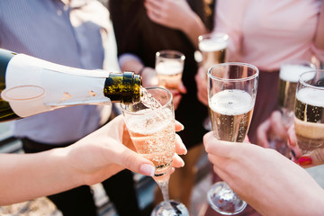 a young company pouring champagne into the wineglasses. young guys drink champagne at sunset. sparkling champagne in glass goblets. splashes of champagne