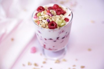 Fototapeta na wymiar Granola yogurt parfait with fresh raspberry berries on a light pink background. Healthy food.