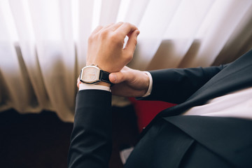 a man in a suit is wearing a watch. a man in a black suit. man looks at the time. man in a business suit. young guy wears wrist watches.