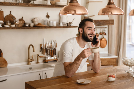 Portrait Of European Brunette Man 20s Drinking Coffee And Using Smartphone At Home