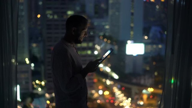 Young man with tablet computer stand by window at home at night