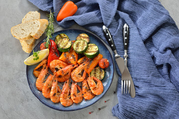 Frische Garnelen vom Grill mit mediterranem Gemüse auf einem blauem Keramikteller auf Tisch mit...