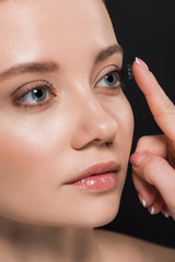 attractive woman attaching contact lens isolated on black