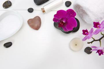 Spa setting with pink orchids, black stones and bath salts on wood background.