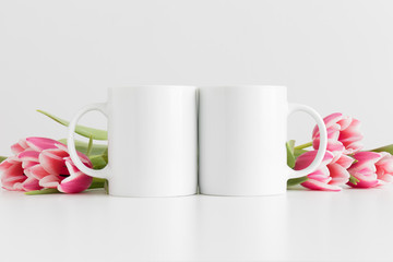 Two mugs mockup with pink tulips on a white table.