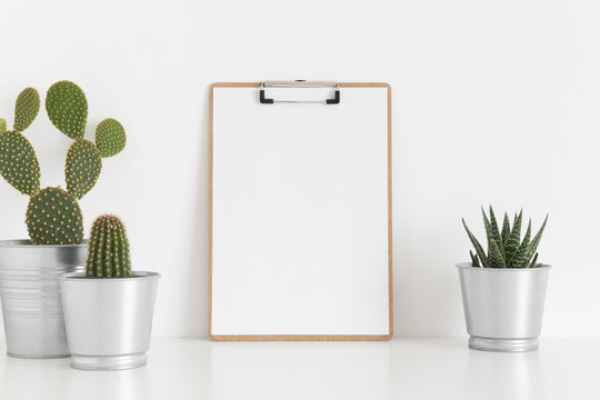 Wooden clipboard mockup with various types of cactus on a white table.