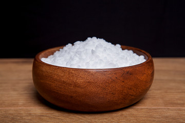 Coarse granules of natural rock or sea salt in a bowls on wooden table.