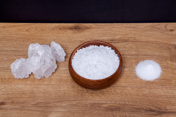 Coarse granules of natural rock or sea salt in a bowls on wooden table.