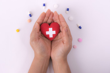 Female hands giving red heart with white cross aymbol on white paper background. International Nurses Day. Healthcare and medical concept.