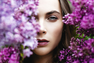 Outdoor fashion photo of attractive young woman surrounded by lilac.