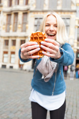 Young beautiful woman holding a traditional Belgian waffle on the background of the Great Market Square in Brussels, Belgium