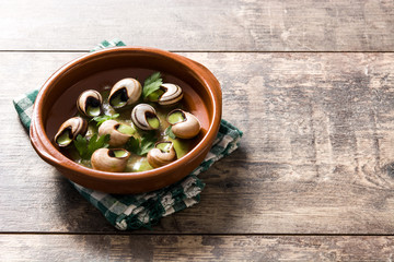 Escargots de Bourgogne in brown bowl on wooden table. Copyspace