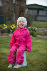 Fototapeta premium Little girl sitting on a bucket in a garden making faces