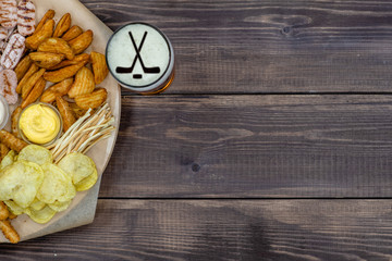 Diverse snacks and beer with silhouettes of hockey sticks on beer foam on dark wooden background....
