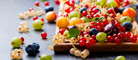 Assortment of fresh berries on wooden cutting board. Slate background. Close up.