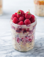 Overnight oats, bircher muesli with raspberry in a glass jar on marble background. Close up.