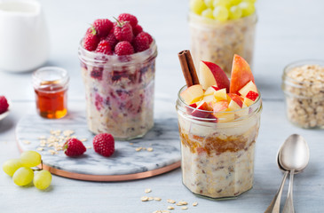 Overnight oats, bircher muesli with raspberry, apple in glass jars on wooden background.