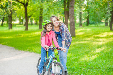 Happy family in the summer park. Mother teaches her daughter to ride a bicycle in the park