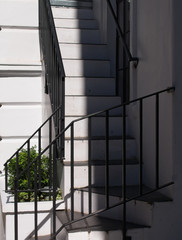 White staircase with black iron handrails. Bright sunlight and shadow.