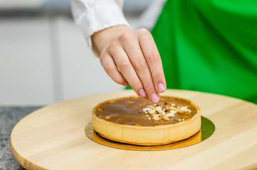 Close up chef sprinkles nuts on a tart at kitchen