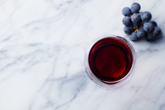 Red wine in glass with fresh grape on marble table background. Top view. Copy space.