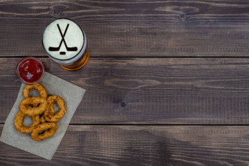 Snacks and beer with silhouettes of hockey sticks on beer foam on dark wooden background. Top view. Empty space for text