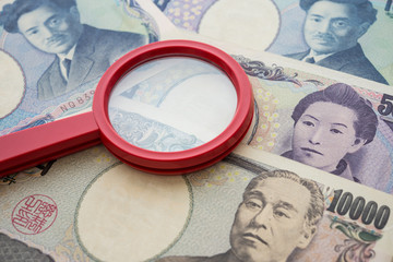 Red magnifying glass on Japanese yen paper banknote bill background. Concept of find out refinance,...