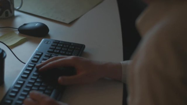 Handheld, medium close up shot of a person typing on a keyboard and using a computer mouse.