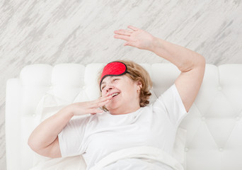 Senior woman sitting on her bed in the morning with arms raised in a stretch
