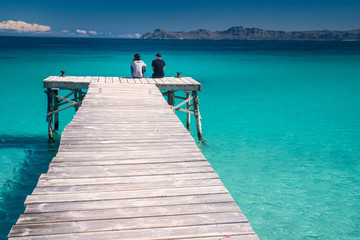 Man and woman sitting together on the pier in beautiful tropical sea. Playa de Muro, Spain.