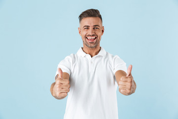 Fototapeta premium Handsome excited emotional adult man posing isolated over blue wall background showing thumbs up.