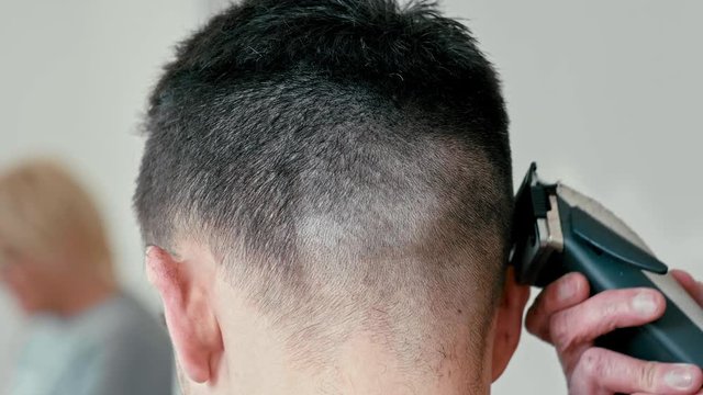 Female Hairdresser is Working and Cutting Hair by Clipper on Back of Head of Young Caucasian Brown-haired Man in Hairdressing Salon or Barbershop. Close Up 4K Slow Motion shot Backside view