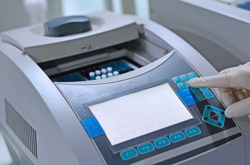 Scientist holding PCR tube put into PCR machine