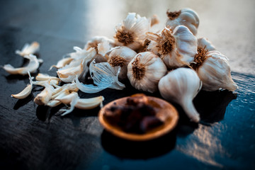 Fresh garlic bulbs or lasun on wooden surface along with some fried garlic cloves in small plate.Used to treat cholesterol.