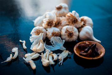 Fresh garlic bulbs or lasun on wooden surface along with some fried garlic cloves in small plate.Used to treat cholesterol.