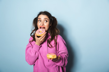 Portrait of attractive young woman with two ponytails smiling while eating sweet donuts