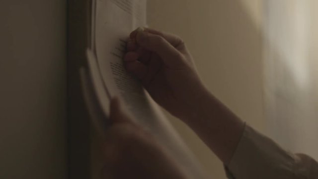 Handheld, close up shot of hands tacking up paper on a bulletin board.