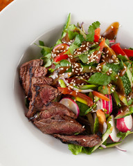 Close-up salad with grilled pork steak on a white plate
