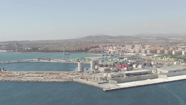 Pre-graded log/flat footage of an aerial moving view of the commercial port of Alicante in the mediterranean coast of Spain.