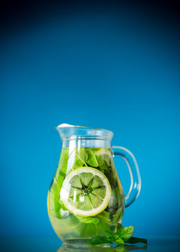 Fresh cold lemonade with lemons and mint in a carafe isolated on blue