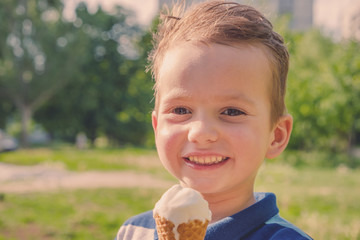 little caucasian boy enjoying a melting ice cream on a sweltering hot summer day. Green summer trees in background