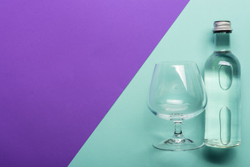 transparent wineglass and bottle with water on bright purple and azure background  